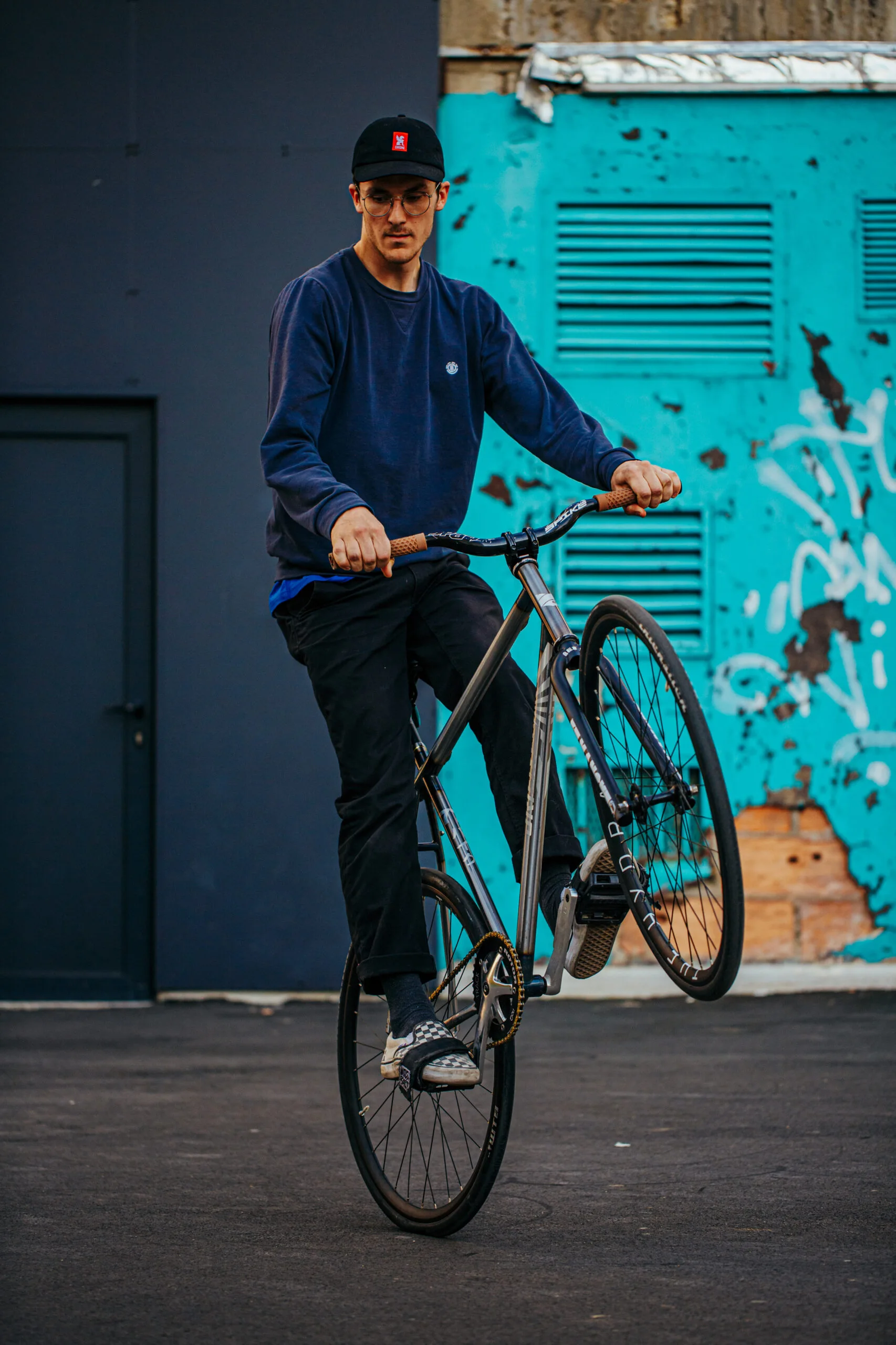 El Fakijoe balancing on his fixed gear bike in front of a turquoise doorway