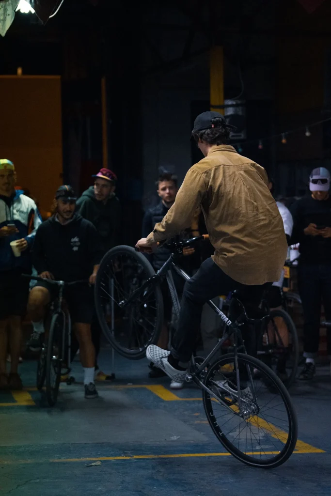 A fixed gear rider lifting the front wheel during a night session, surrounded by other riders
