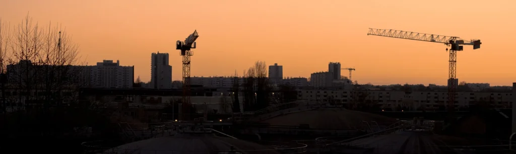 Paris rooftops and cranes silhouetted against a deep orange evening sky