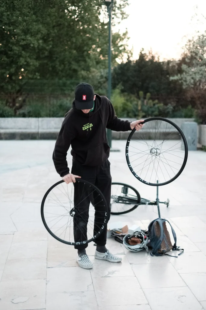 Person holding a wheel beside a bicycle and tools on the riverbank.
