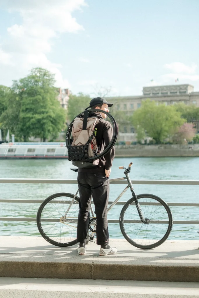 Rider standing with a fixed gear bike beside the Seine.
