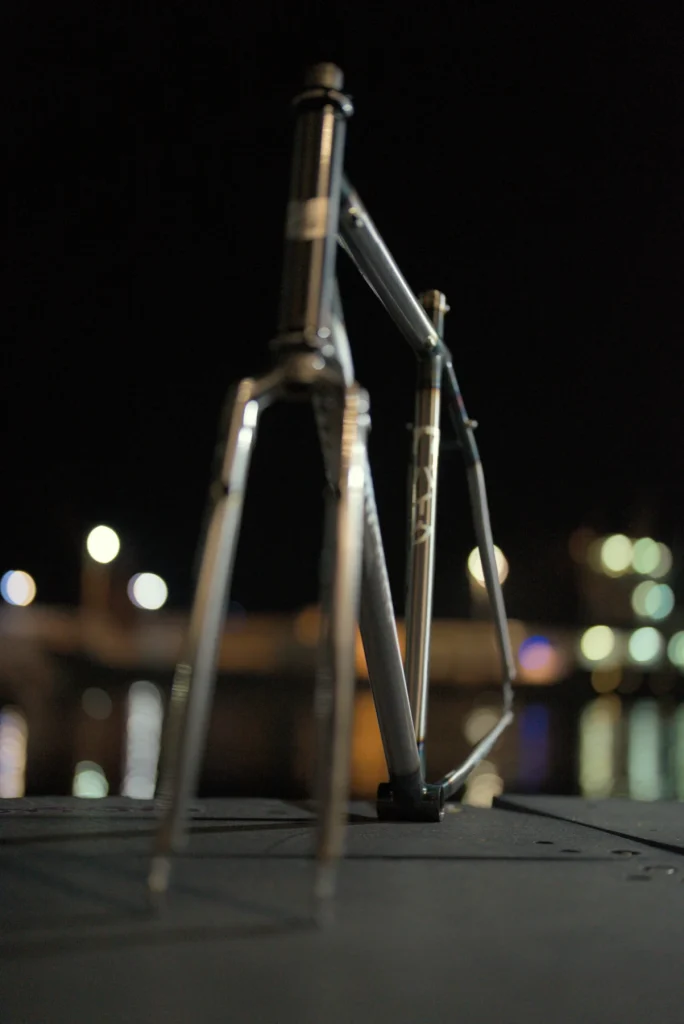 Rear view of the raw steel JRI Grit frame, with the seat cluster in focus against night lights
