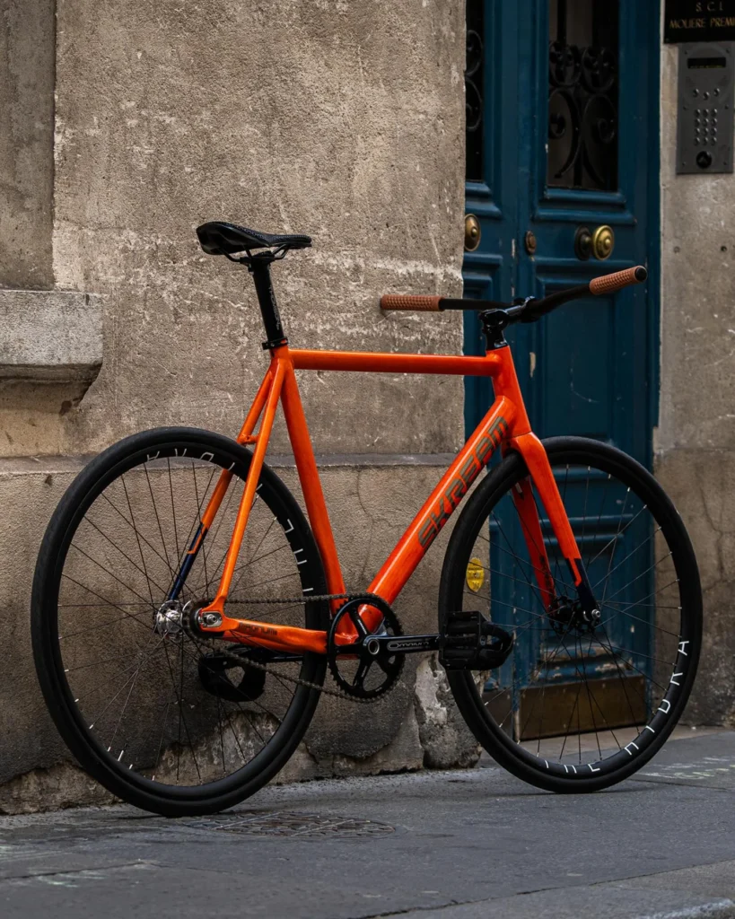 The orange Skream Magnum24 Lava bicycle against a stone wall and blue doorway