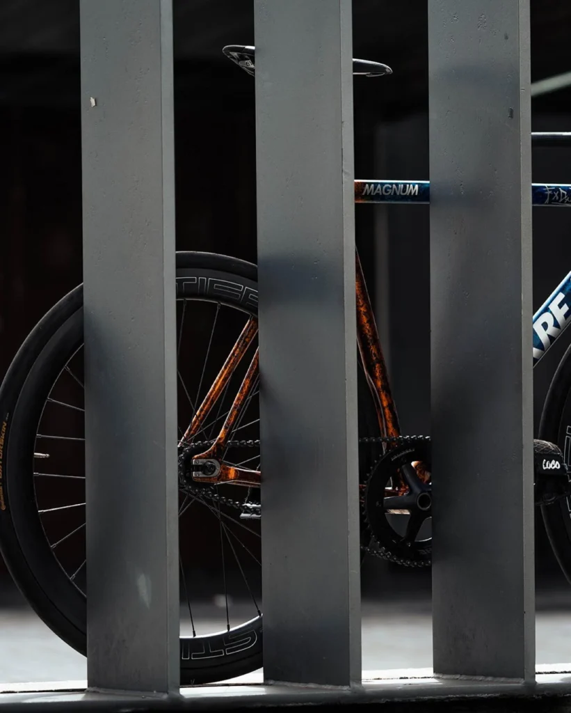 Orange rear triangle and deep section rear wheel seen through grey metal bars