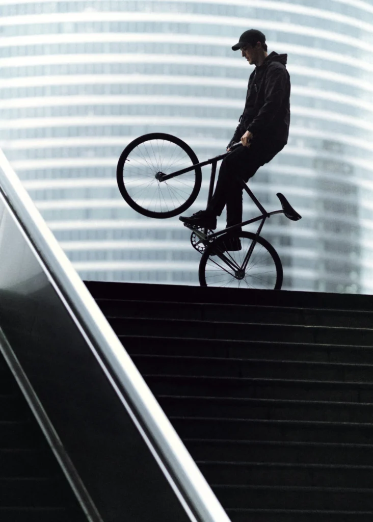 El Fakijoe balancing a wheelie on a stairway under sculptural white lights